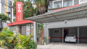 Entrada de un hotel con un letrero rojo y blanco, una zona de estacionamiento techada y un coche blanco estacionado adentro.