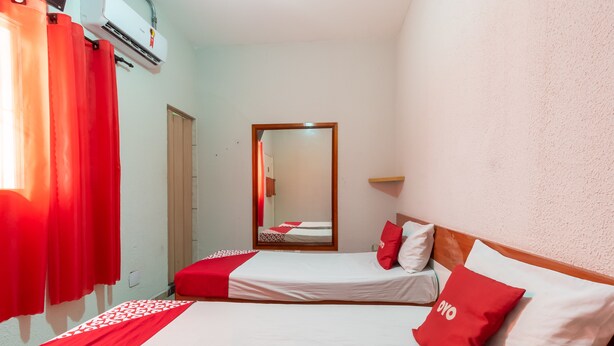 Habitación de hotel con dos camas, ropa de cama roja y blanca, un espejo y una pequeña estantería.