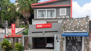Entrada de un hotel con fachada roja y gris, un letrero que dice "OYO HOTEL DOM PEDRO" y un estacionamiento con un coche.