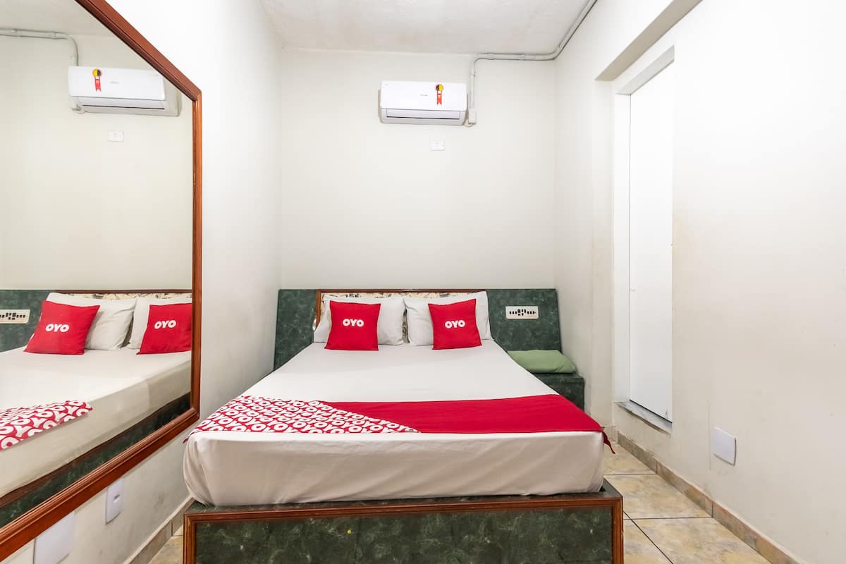 Een hotelkamer met een bed, een spiegel, een airconditioning en een raam.