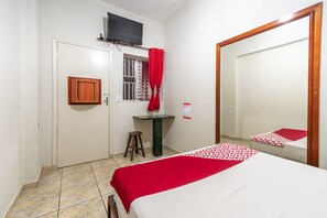 A bedroom with a bed, a small table, a mirror, a TV, and a window with curtains. - OYO Hotel Dom Pedro, São Paulo (São Paulo)