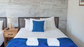 A hotel room with a bed, a nightstand with a lamp, and a folded towel on the bed. - Maison Lebreux - Motel (Petite-Vallee)