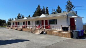 A row of single-story cabins with red doors and windows, a covered deck area, and a clear sky. - Maison Lebreux - Motel (Petite-Vallee)