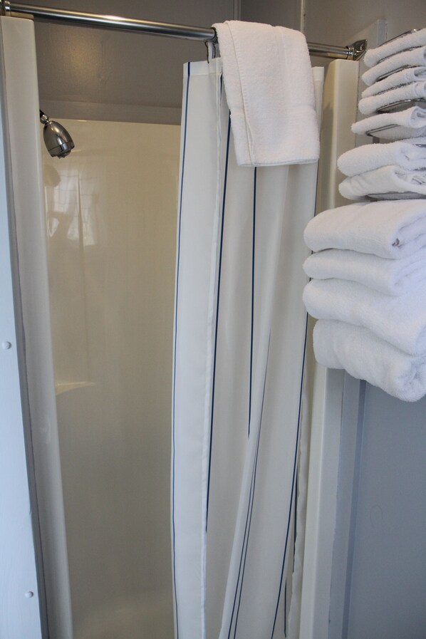 A shower area with a glass door, a metal towel rack, and a stack of folded towels. - Maison Lebreux - Motel (Petite-Vallee)