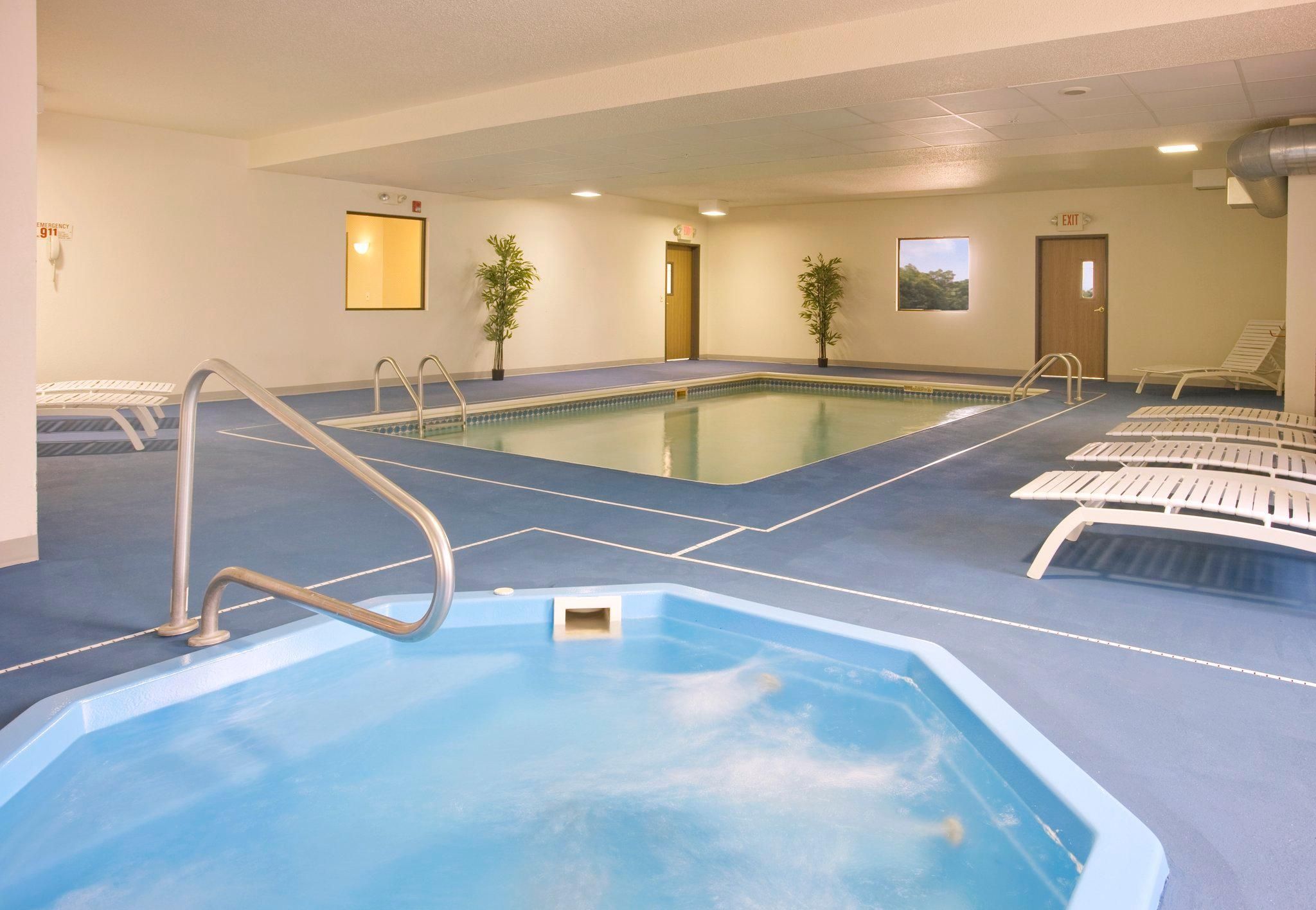 An indoor swimming pool with a blue floor, a lifeguard chair, and a door marked 'EXIT'.