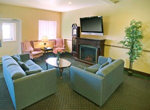 A hotel room with a fireplace, a television mounted above it, a sofa set, a table with a vase of flowers, and a potted plant. - Americas Best Value Inn Gaylord (Gaylord)
