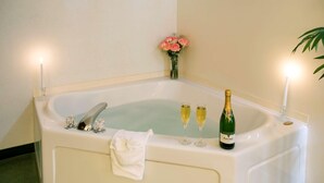 Une grande baignoire avec des coupes à champagne et une bouteille, une serviette blanche et un vase de fleurs.