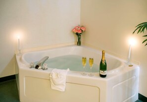 Una bañera grande con copas de champán y una botella, una toalla blanca y un jarrón con flores.