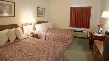 A hotel room with two beds, a desk with a laptop, a TV, a window with curtains, and a framed picture on the wall.