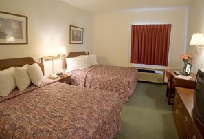 A hotel room with two beds, a desk with a laptop, a TV, a window with curtains, and a framed picture on the wall.