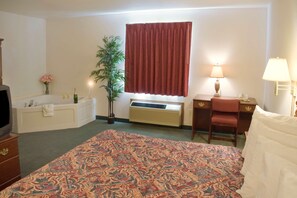 A hotel room with a large bed, a desk, a chair, a television, a bathtub, and a window with curtains. - Americas Best Value Inn Gaylord (Gaylord)