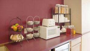 Un plan de travail de cuisine avec un panier de fruits, une machine à café et des boîtes de rangement.