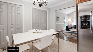Une cuisine moderne avec un réfrigérateur en acier inoxydable, une table à manger avec des chaises blanches et un lustre.