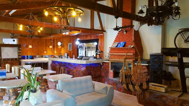 Un rústico espacio bar con paredes de madera, una barra de piedra y una chimenea de ladrillo. Hay mesas y sillas para sentarse, y se ve un teclado Yamaha.