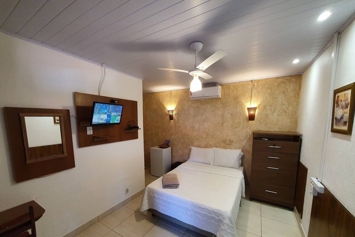 A hotel room with a bed, a TV mounted on the wall, a ceiling fan, and a dresser.