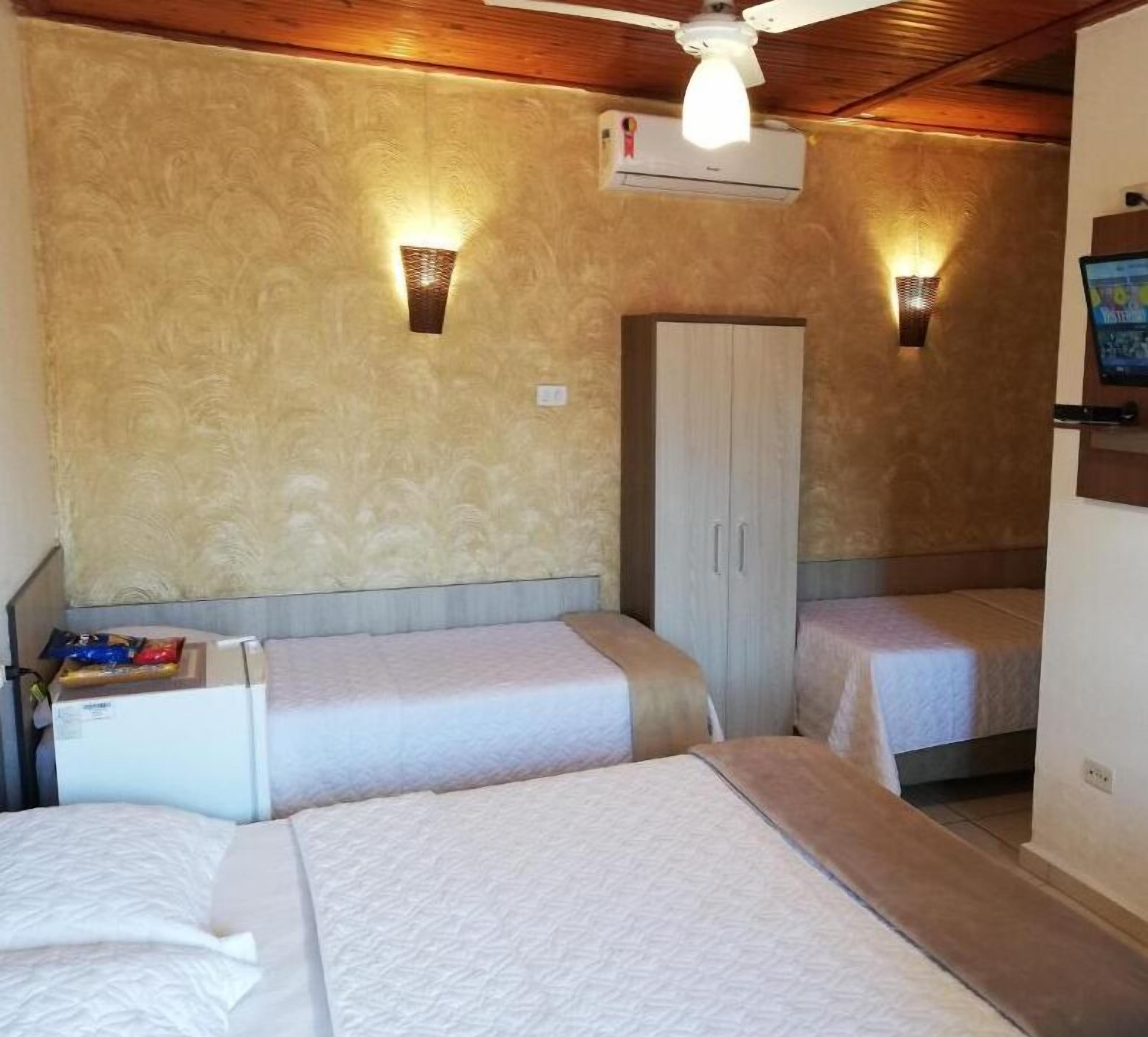 A room with two beds, a wardrobe, a ceiling fan, and an air conditioning unit.