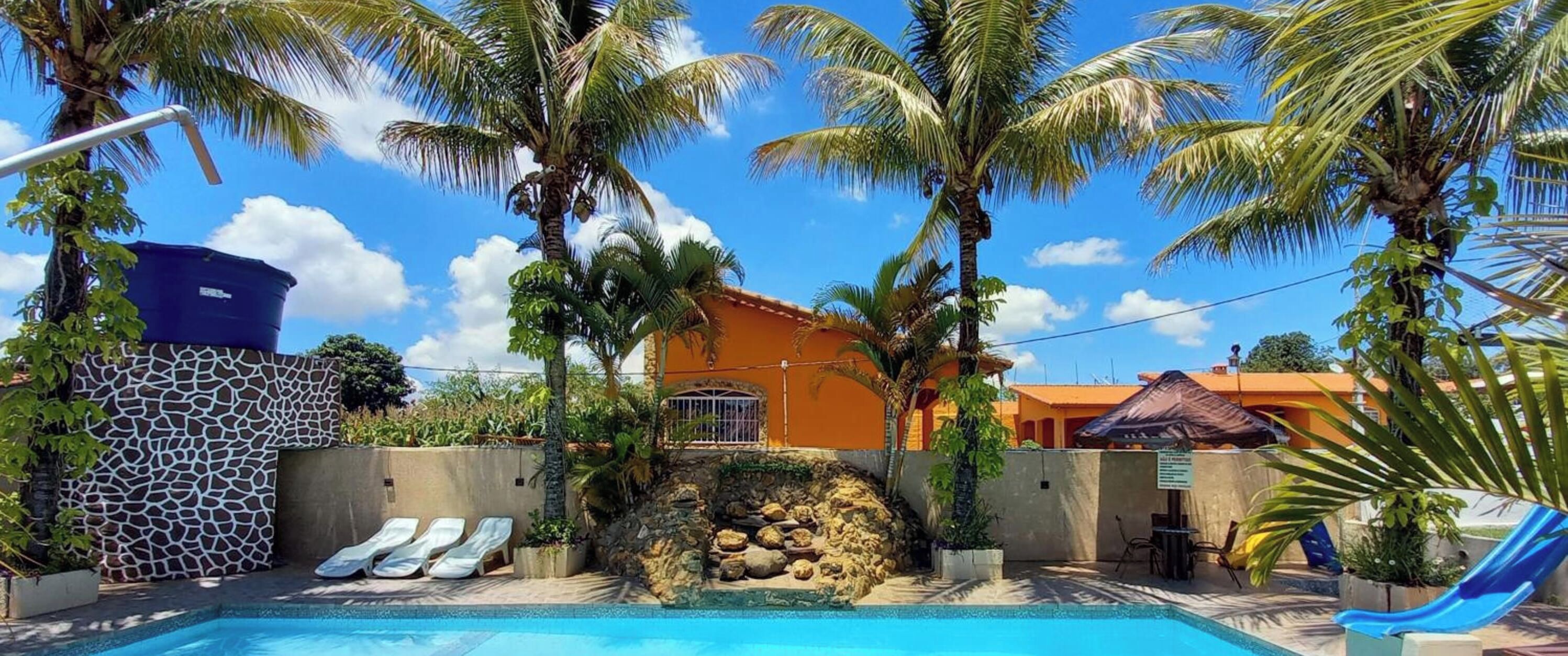 Un área de piscina con sillones de descanso, palmeras y un edificio con pared de piedra.