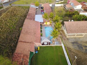 Vista aérea de una zona residencial con piscina, patio cercado y un edificio con techo de tejas rojas.