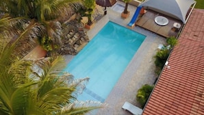 Vista aérea de una piscina rodeada de palmeras y una zona cubierta con asientos.