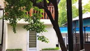 A building with a white exterior, a wooden fence, and a stone planter with grass. - Park Hostel Osh (Osh)