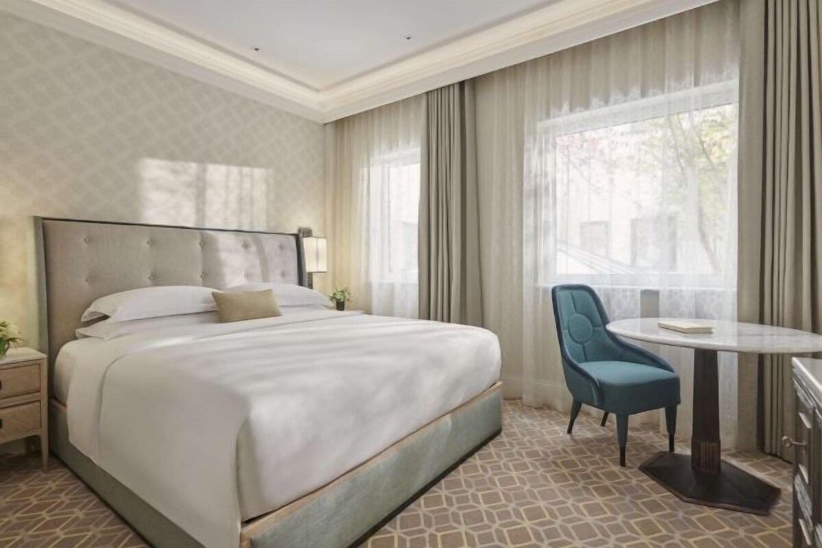 A hotel room with a large bed, a bedside table, a chair, and a window with curtains.