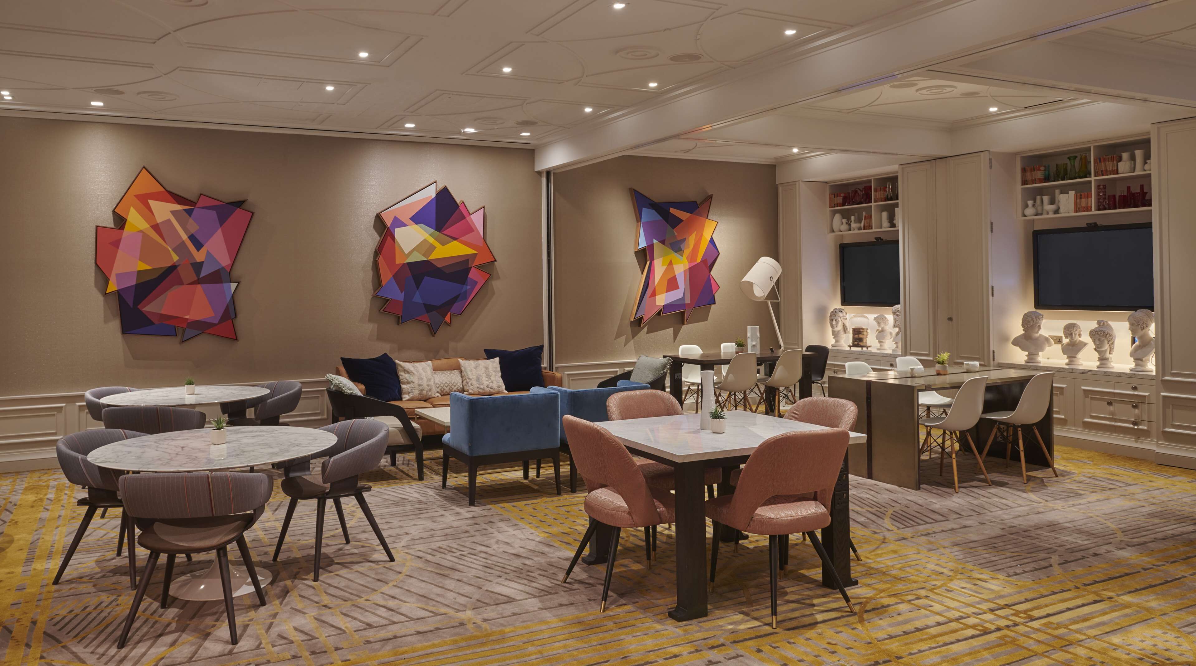 A modern dining area with round tables and chairs, abstract art on the walls, and a television above a shelf with busts.