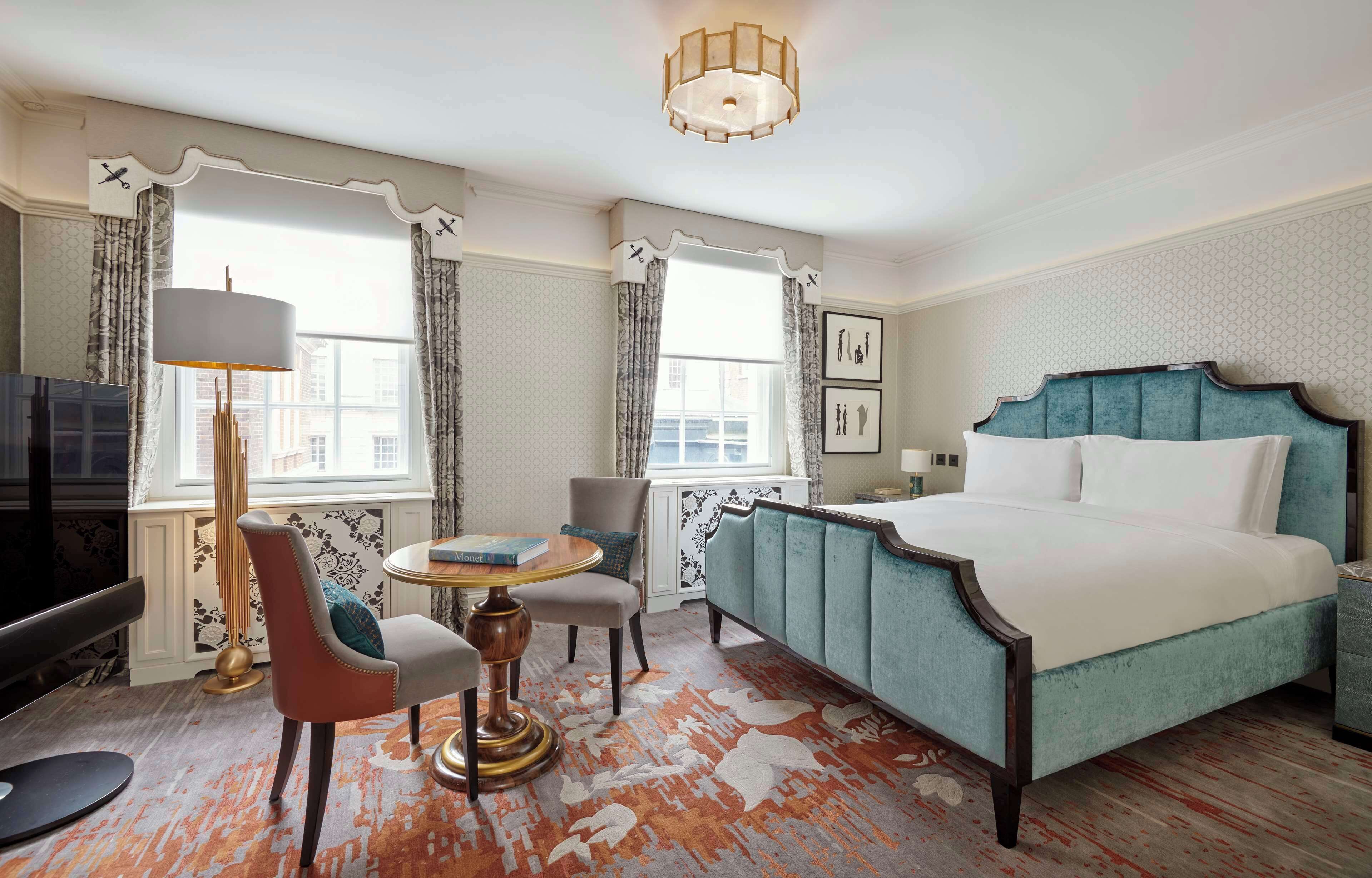 A hotel room with a bed, a desk, a chair, a lamp, and a television.