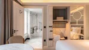 A modern hotel room with a marble bathroom, a round mirror, and a neatly made bed.