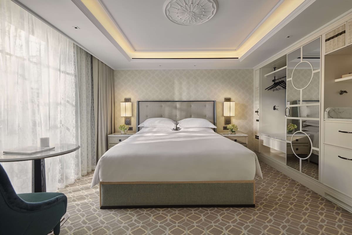 Une chambre d’hôtel moderne avec un grand lit, des lampes de chevet, un miroir rond, une armoire avec des étagères et une petite table avec une chaise.