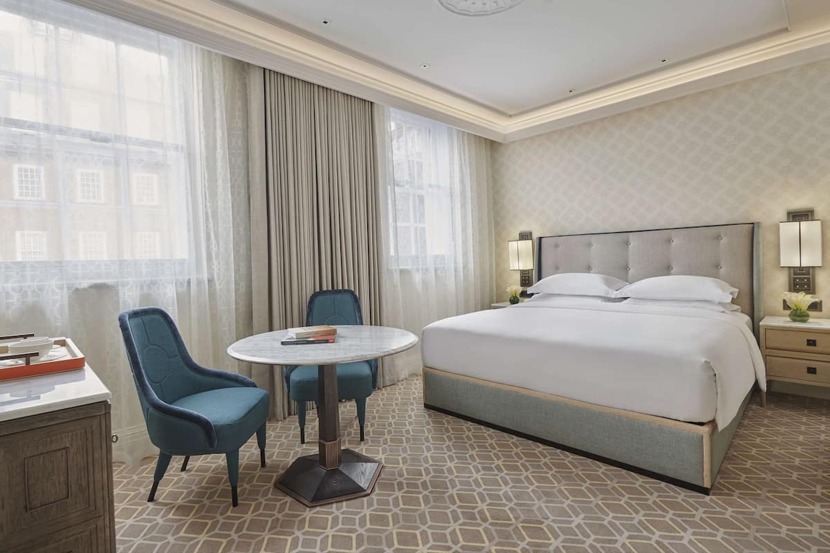 Une chambre d’hôtel avec un grand lit, une table ronde avec deux chaises, un bureau avec une chaise et une table de chevet avec une lampe.