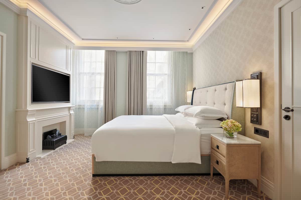 Une chambre d’hôtel avec un grand lit, une télévision à écran plat, une table de chevet avec une lampe et une cheminée.