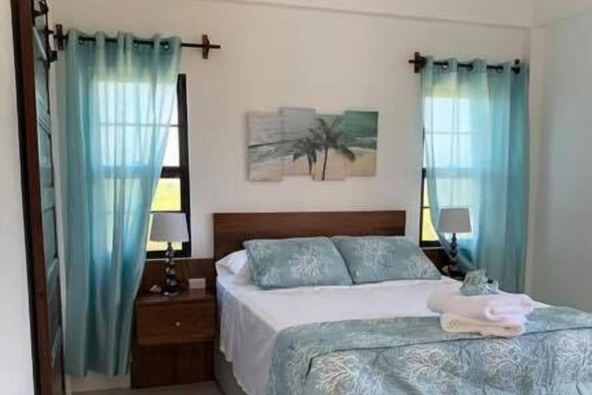 Een slaapkamer met een bed, nachtkastjes, een plafondventilator en een schilderij aan de muur.