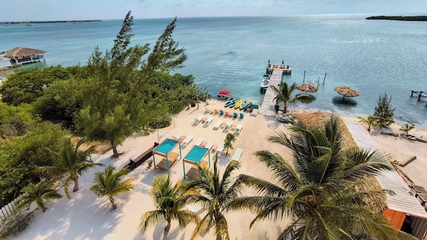 A beach with lounge chairs, a pool, and a pier extending into the water. - Bay Towers Hotel (Caye Caulker)