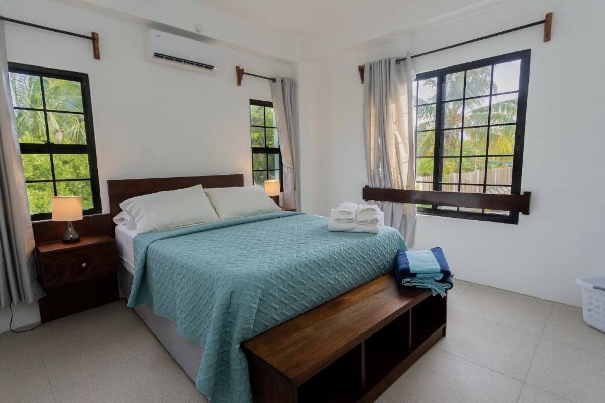 Een slaapkamer met een bed, nachtkastjes, een bankje en een raam met gordijnen.