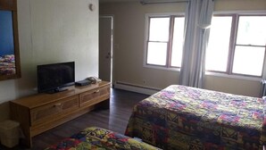 A bedroom with a wooden dresser, a television, a bed with a patterned blanket, and a window with curtains. - Baw Beese Inn (Hillsdale)