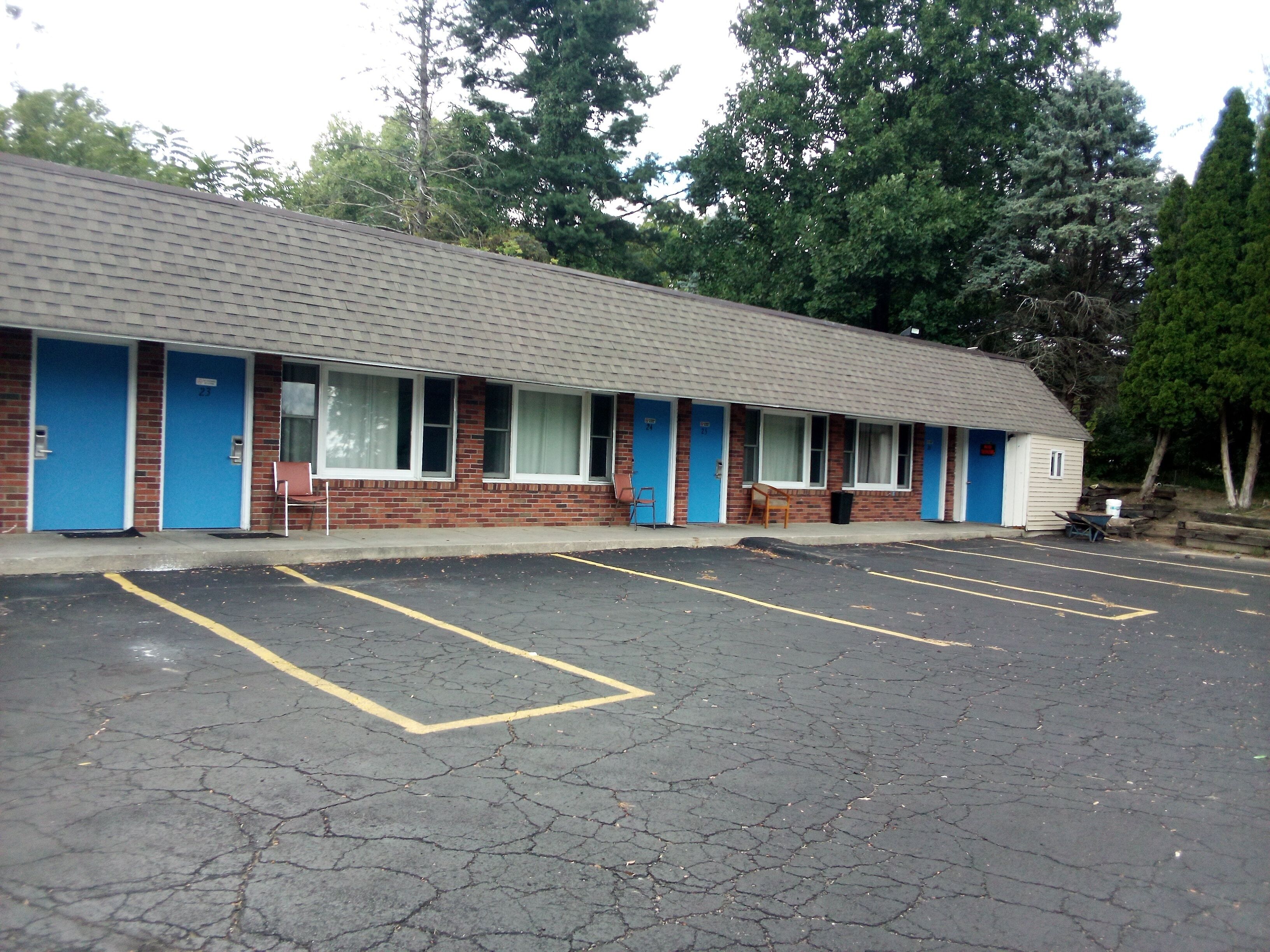 Un motel con puertas azules, números 23 y 24, un estacionamiento con espacios delimitados y fachada de ladrillo.