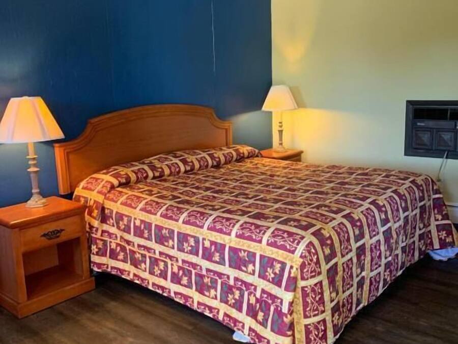 Un dormitorio con una cama de madera, dos mesitas de noche con lámparas y un televisor montado en la pared.