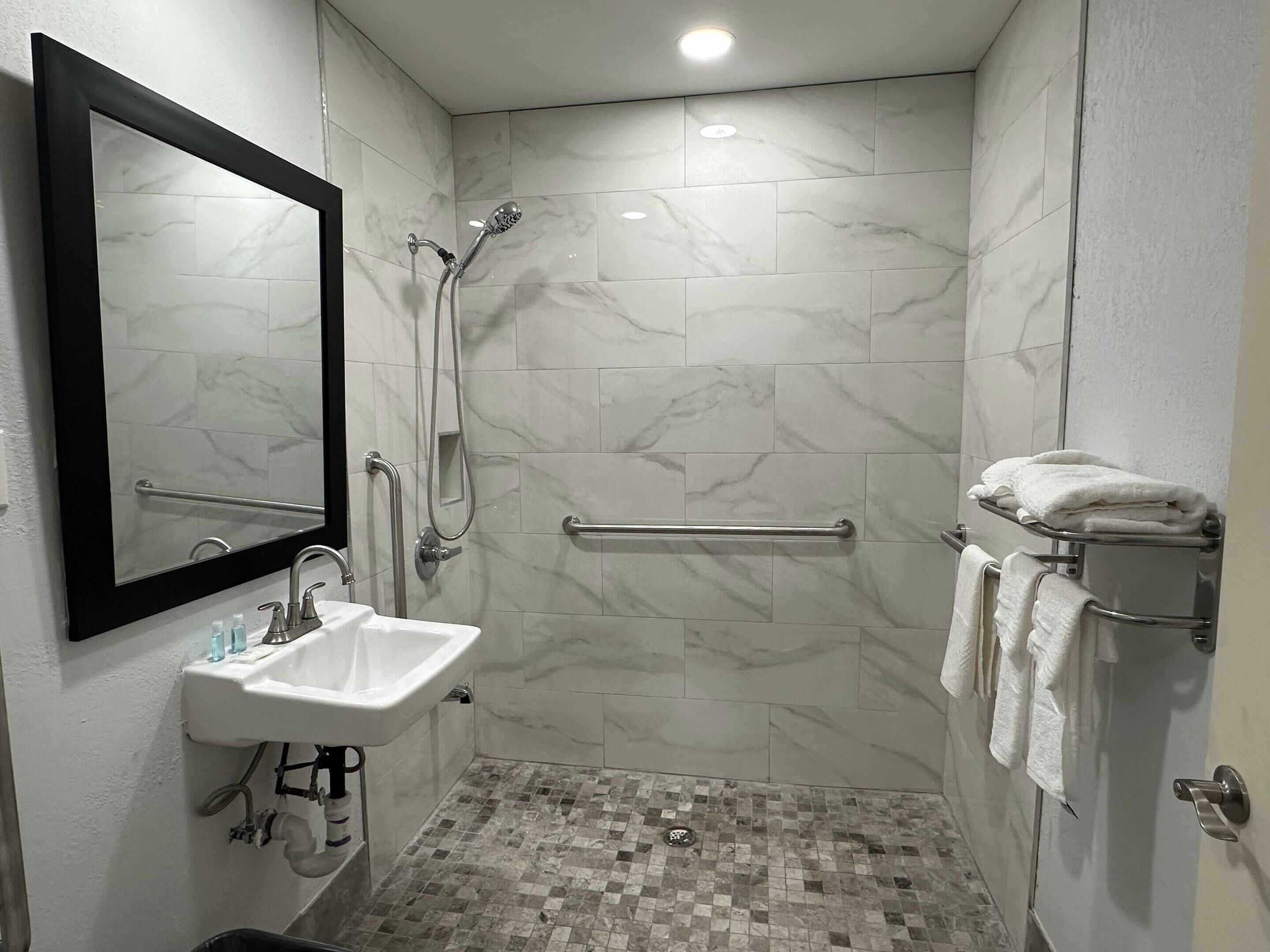 A modern bathroom with a white sink, mirror, shower, and tiled floor.