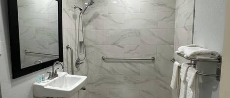 A modern bathroom with a white sink, mirror, shower, and tiled floor.