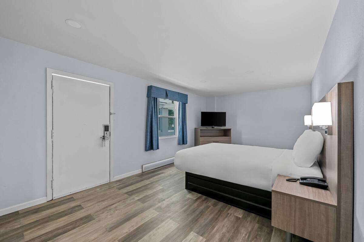 Een hotelkamer met een bed, een televisie, een nachtkastje en een deur.