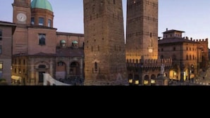 Una plaza histórica con dos torres destacadas y una torre del reloj al fondo.