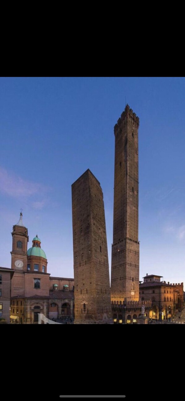 A historic square with two prominent towers and a clock tower in the background. - Verdi Plaza - Hostel (Bologna)
