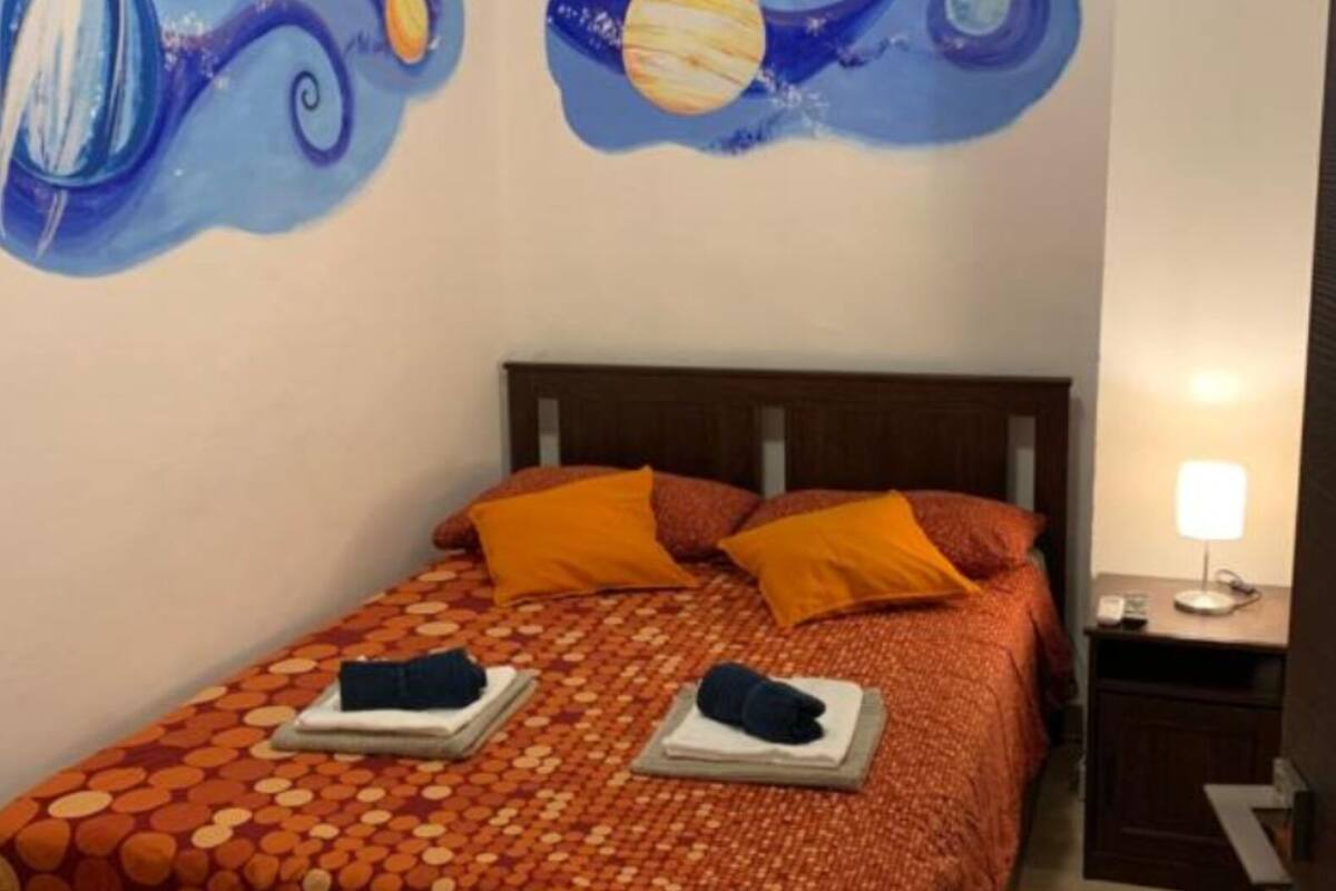 A bedroom with a bed, orange pillows, and a wall mural of planets.