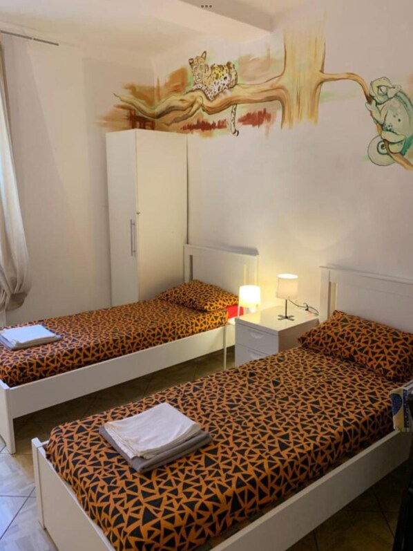 A room with two single beds, a wardrobe, a desk with a lamp, and a wall mural. - Verdi Plaza - Hostel (Bologna)