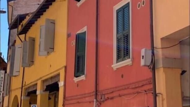 Un edificio de varios pisos con fachada roja y contraventanas verdes, que presenta una escalera visible y un letrero de estacionamiento.