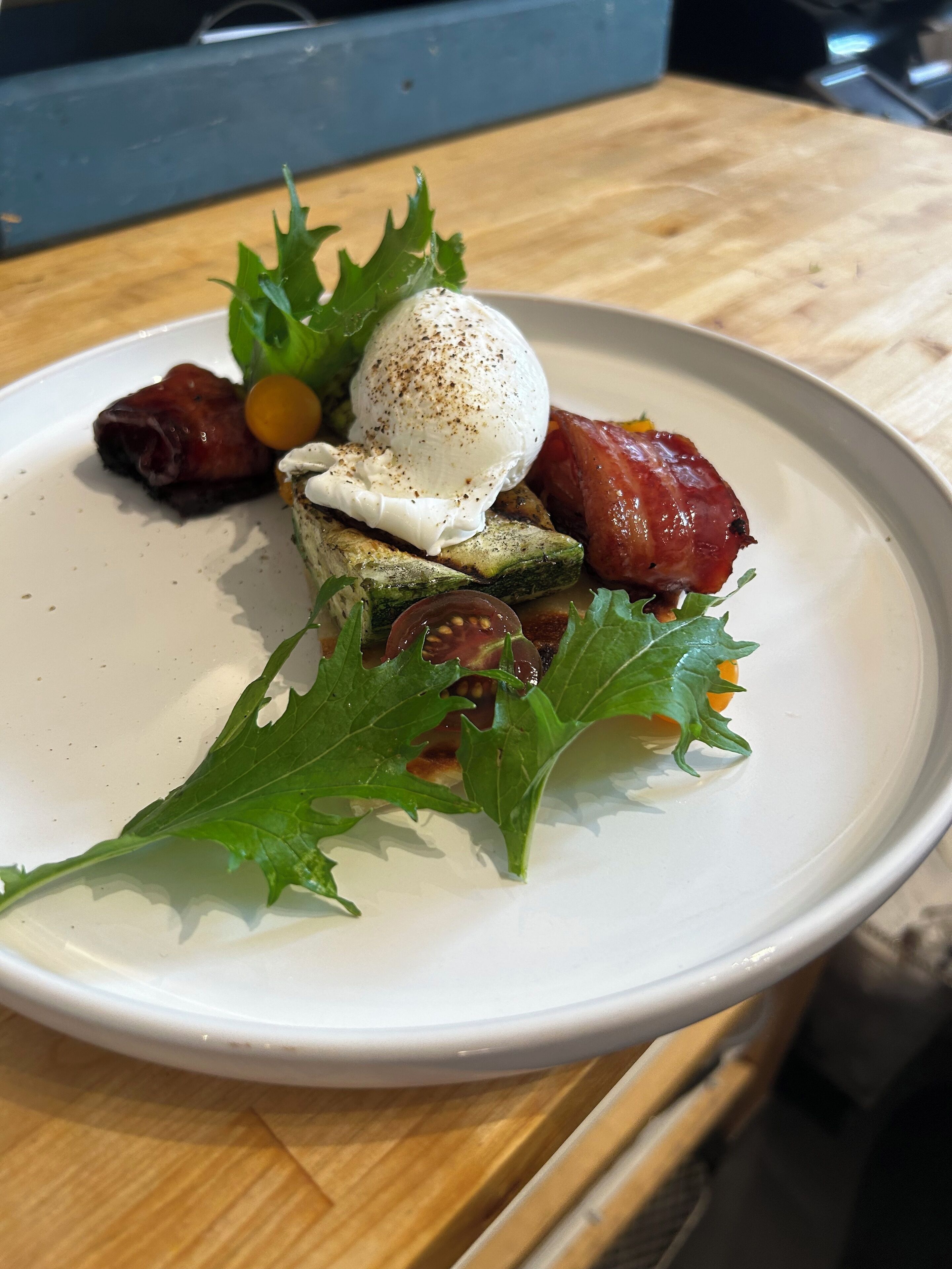 A plate with a poached egg, asparagus, arugula, and bacon on a white plate.