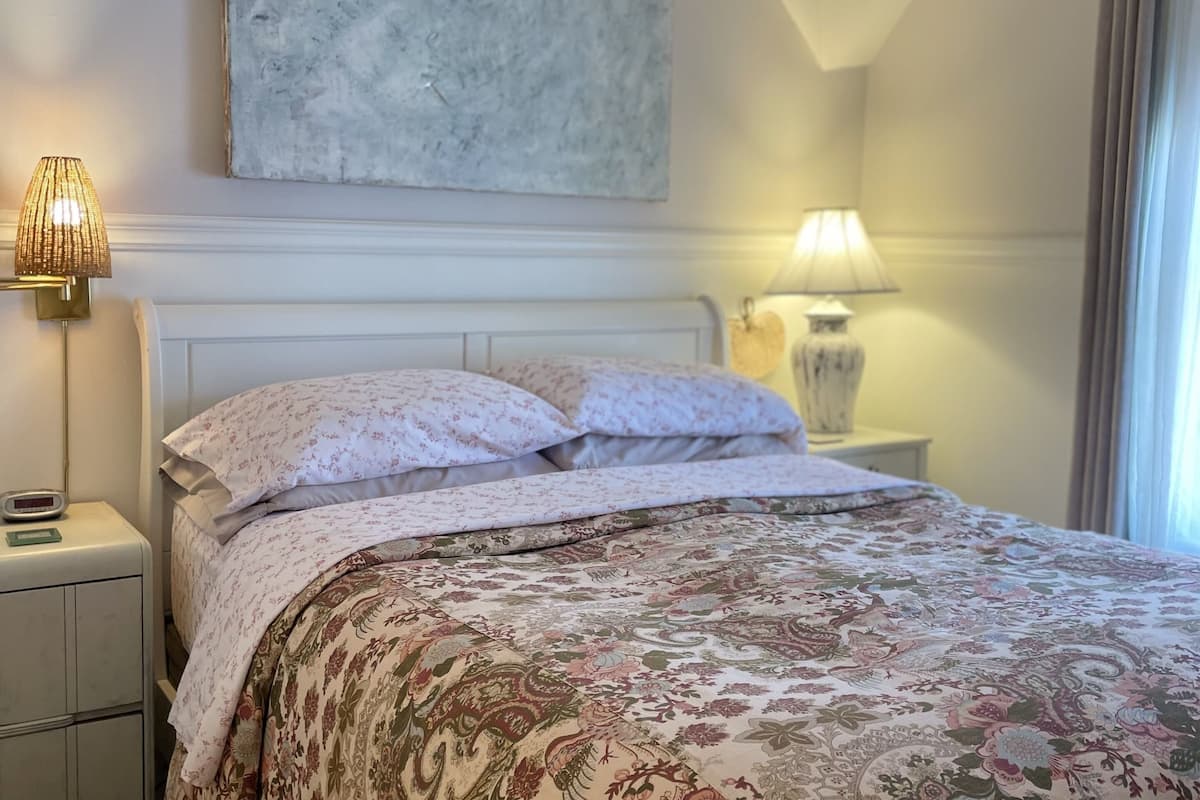 Een hotelkamer met een groot bed, een nachtkastje met een lamp, een wandklok en een schilderij boven het bed.