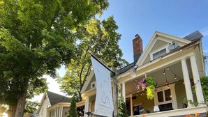 Een tweelaags huis met een veranda, een tuin met verschillende planten en bloemen, en een bordje met 'La Maison de Ville Bed & Breakfast'.