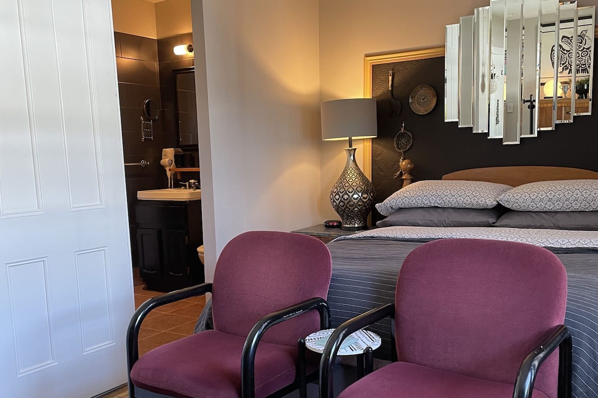 Een hotelkamer met een bed, twee stoelen, een nachtkastje, een lamp en een spiegel aan de muur.