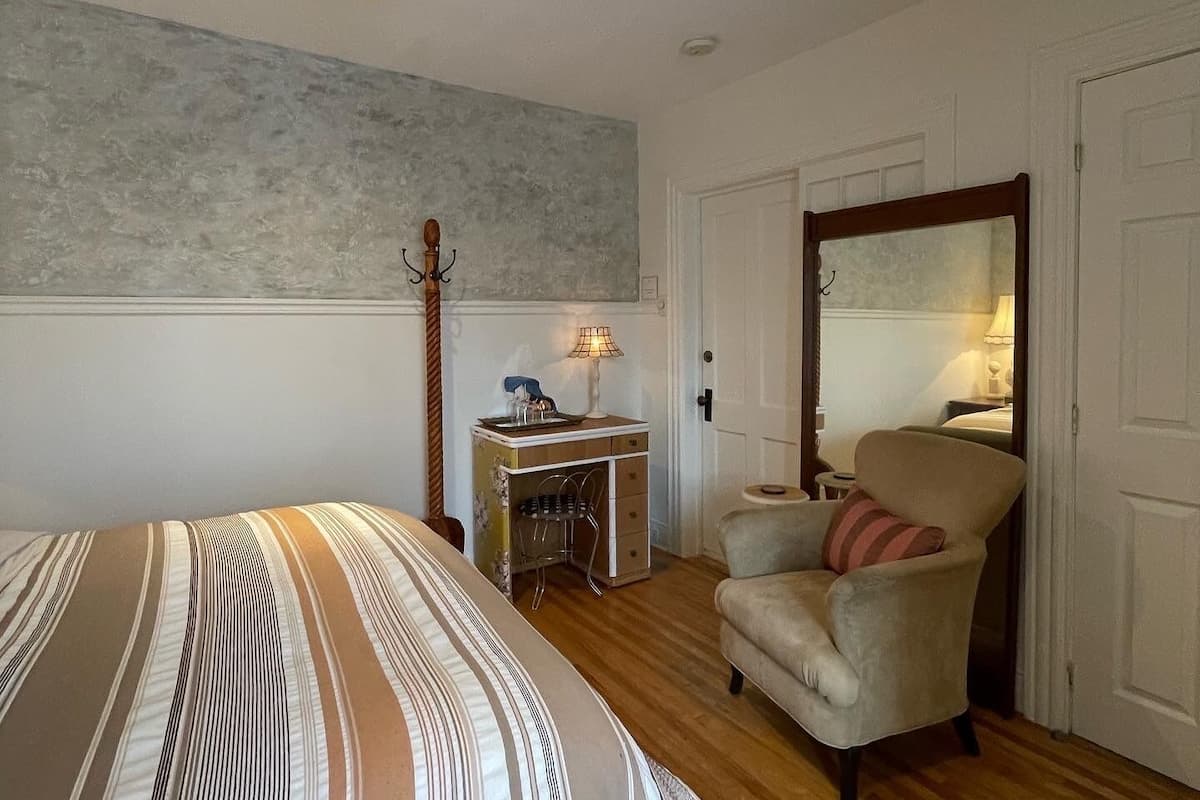 Een slaapkamer met een bed, een stoel, een bureau en een spiegel.